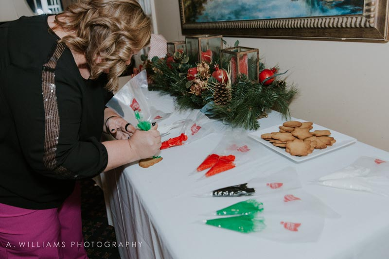 woman decorating cookies at holiday party with green, red, and black frosting piping bags